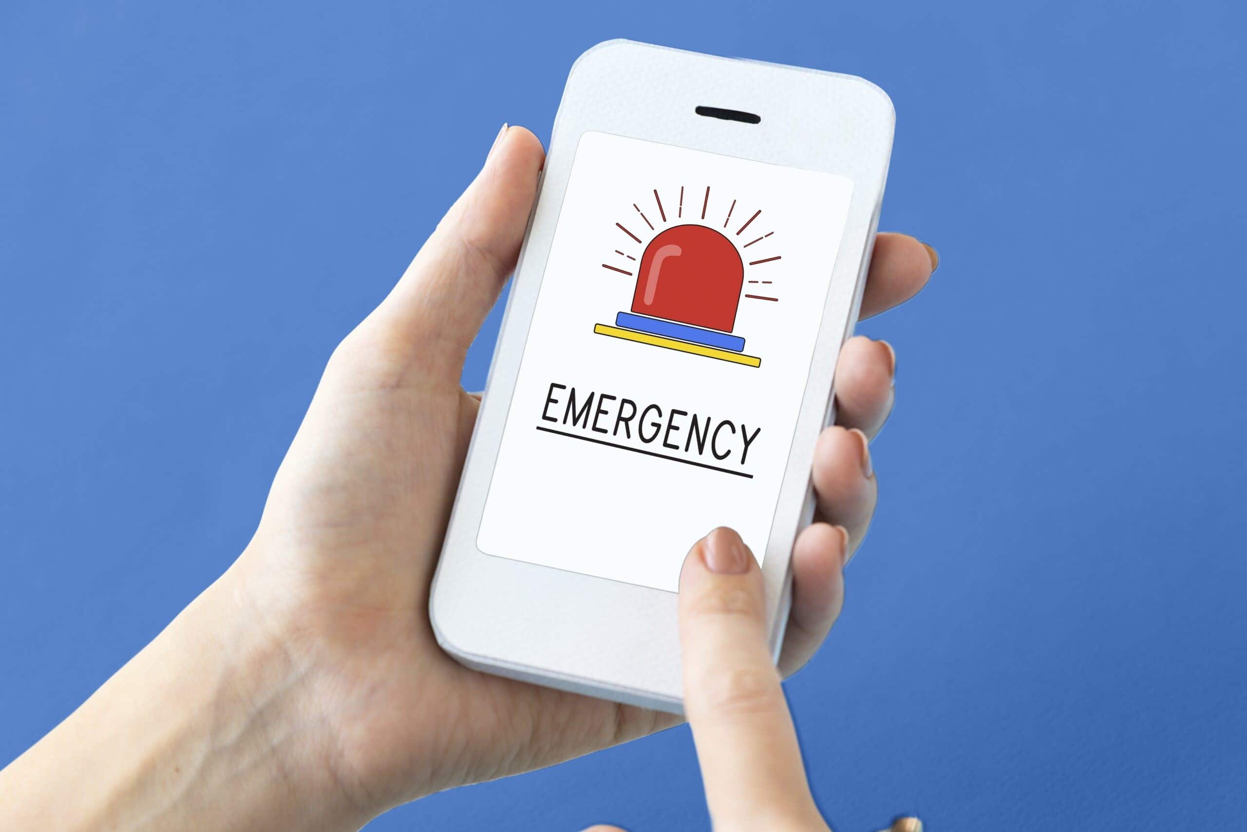 Trivallis Housing Landlord Wales A person is holding a smartphone displaying an emergency alert symbol on the screen against a blue background, related to Trivallis RCT housing.