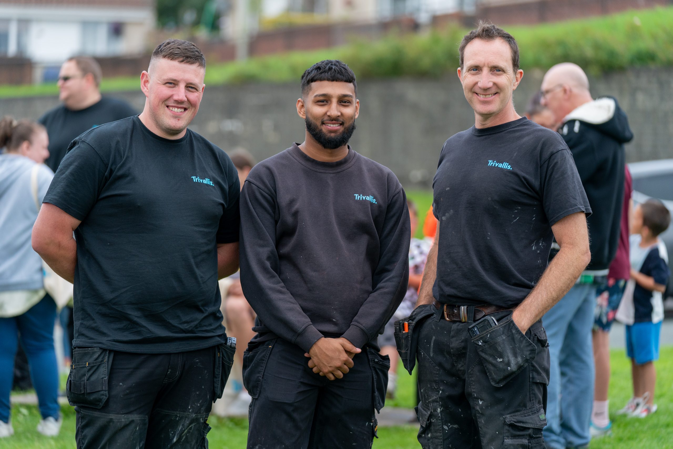 Three smiling men in black work shirts and trousers standing together outdoors.