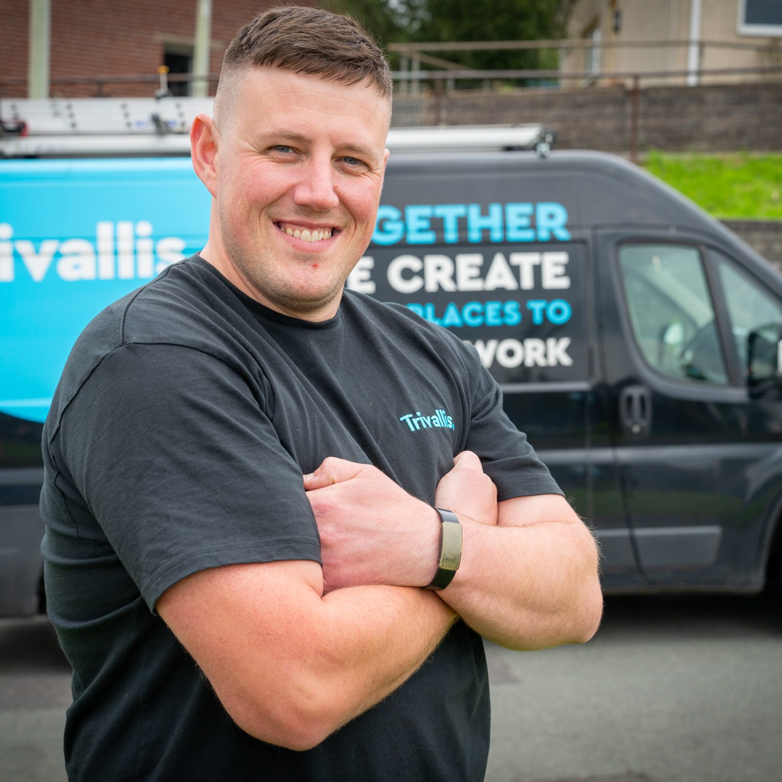 A man with crossed arms smiling in front of a service van with 