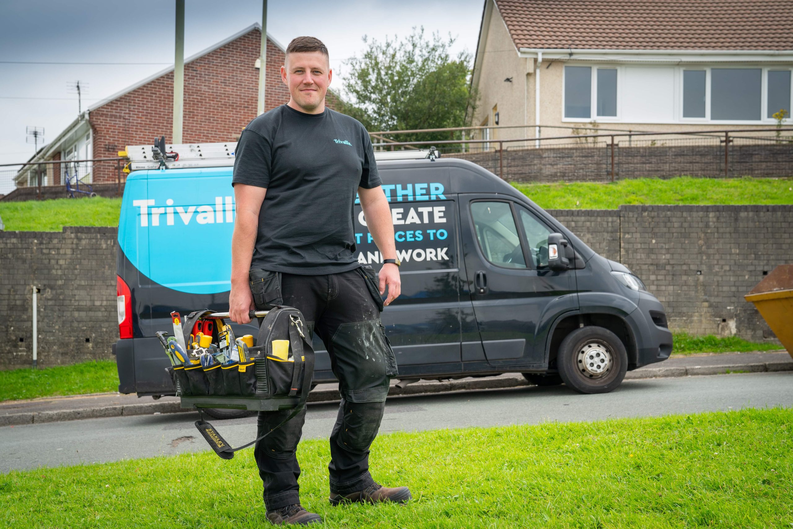 A man carrying a toolbox smiling in front of a service van with 