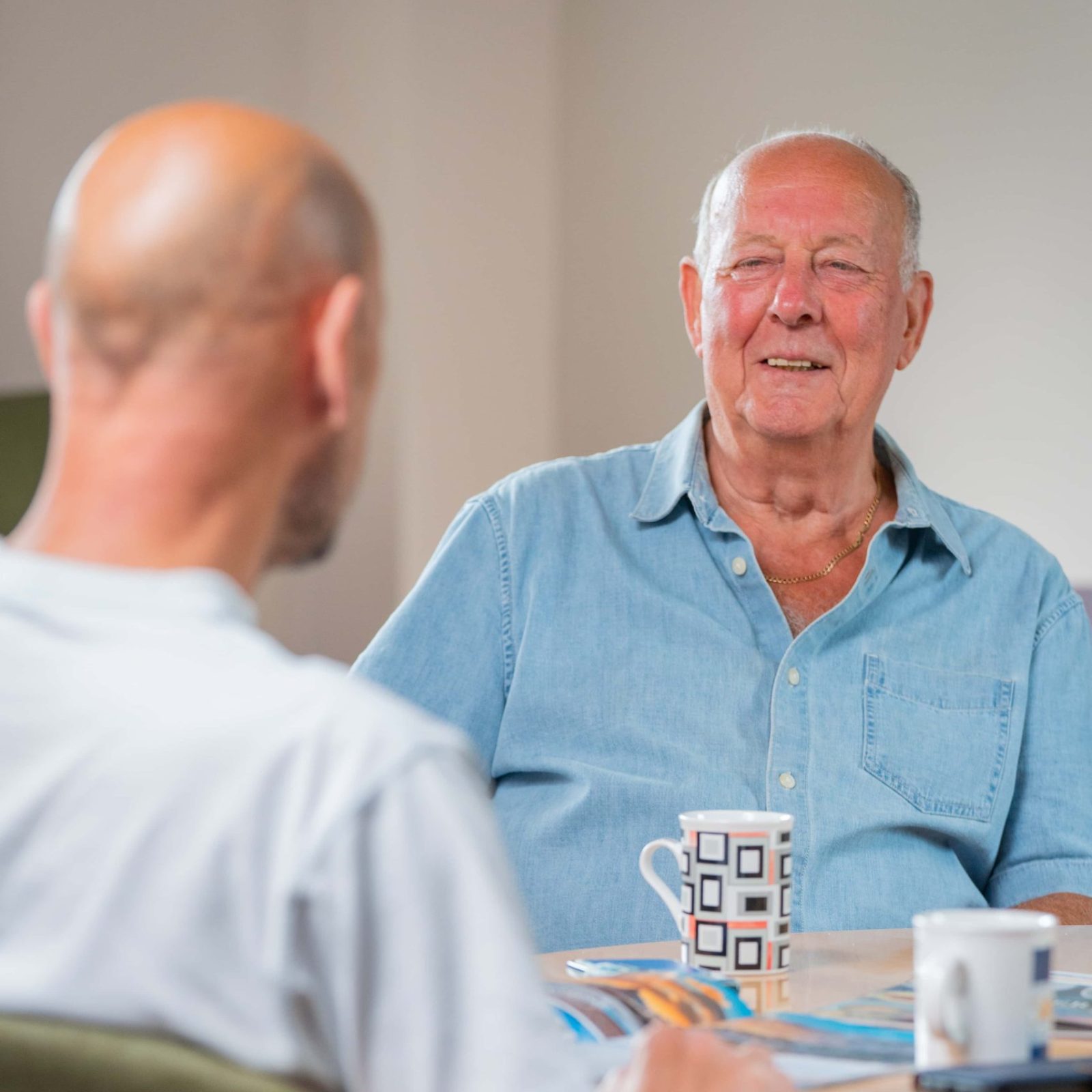 Trivallis Housing Landlord Wales Two men engaged in a conversation about housing while sitting at a table with a mug and some papers between them for the Trivallis RCT project.