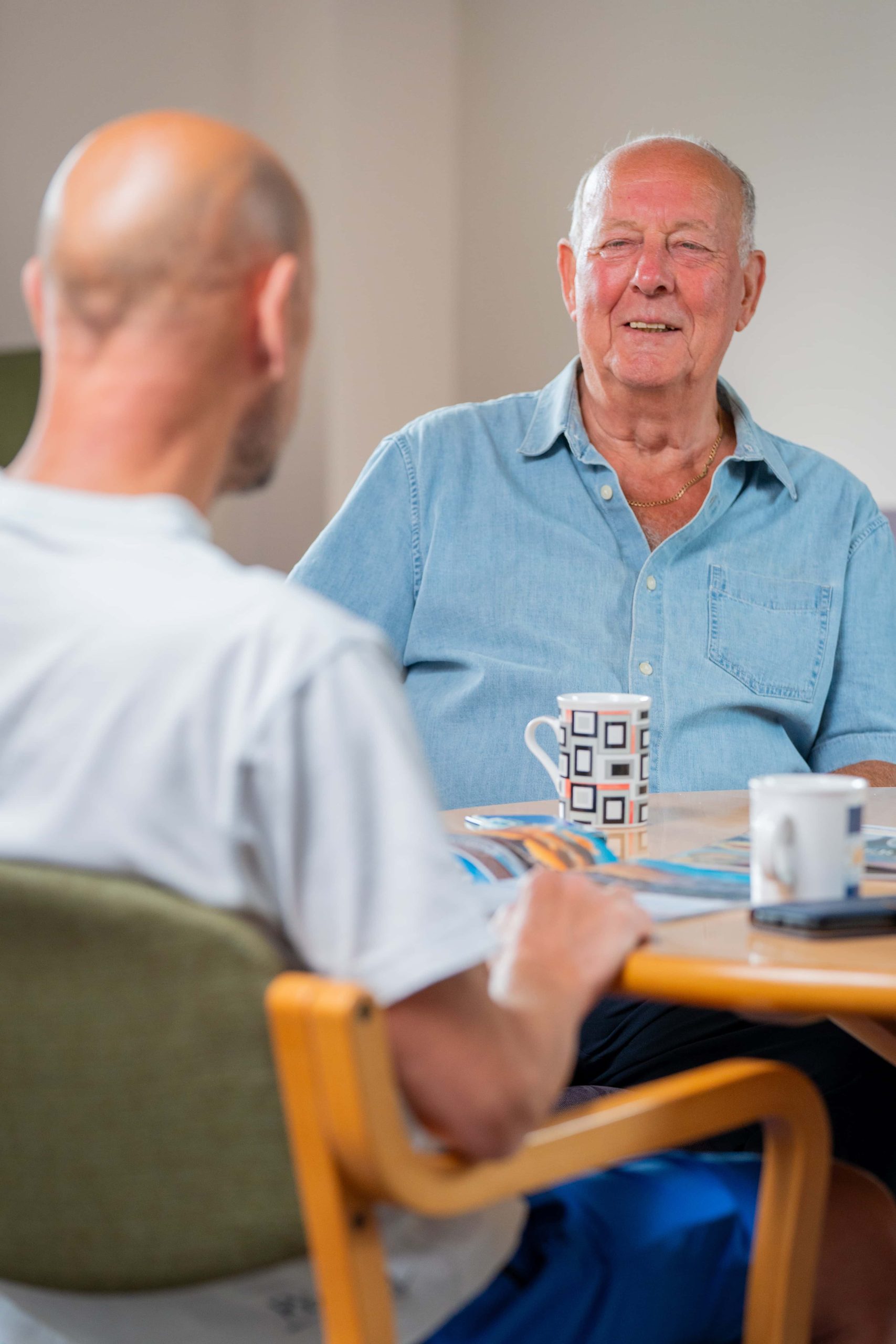 Trivallis Housing Landlord Wales Two men engaged in a conversation about housing while sitting at a table with a mug and some papers between them for the Trivallis RCT project.