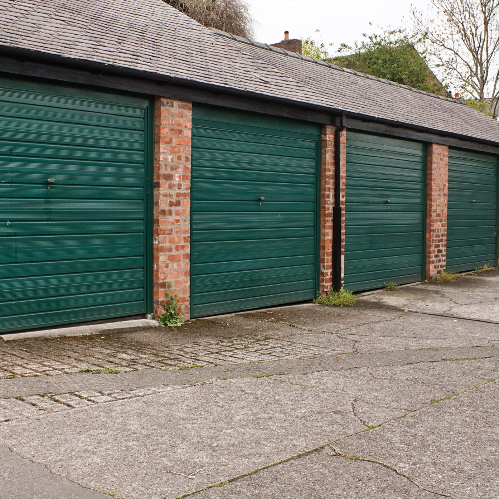 Trivallis Housing Landlord Wales A row of green garages along a Trivallis housing brick building, with a paved area in the foreground.