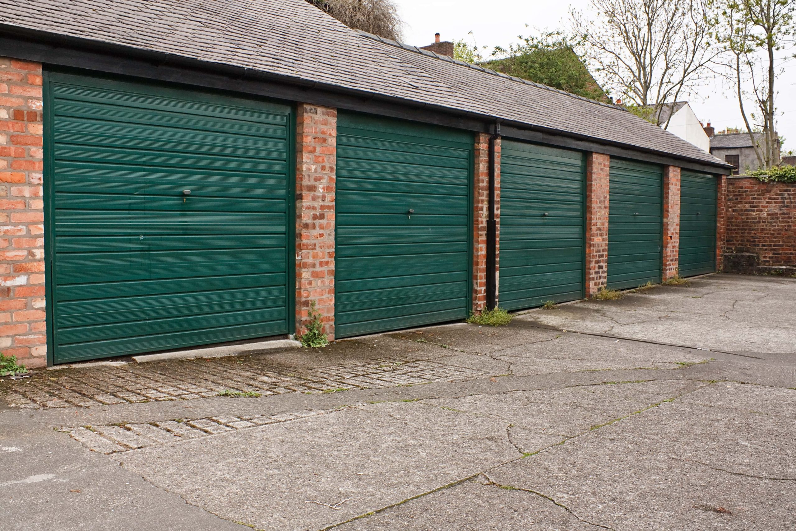 Trivallis Housing Landlord Wales A row of green garages along a Trivallis housing brick building, with a paved area in the foreground.