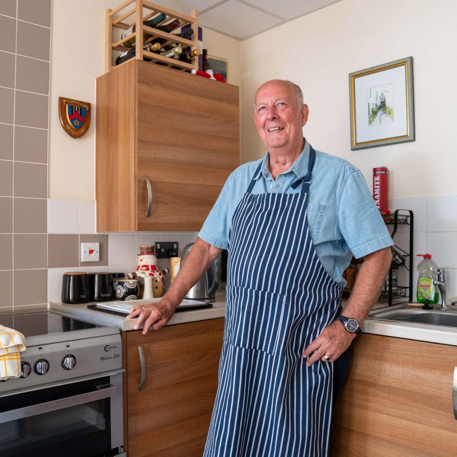 A proud home chef stands with a smile in a well-equipped kitchen, wearing a striped apron and poised for a session of culinary creation.