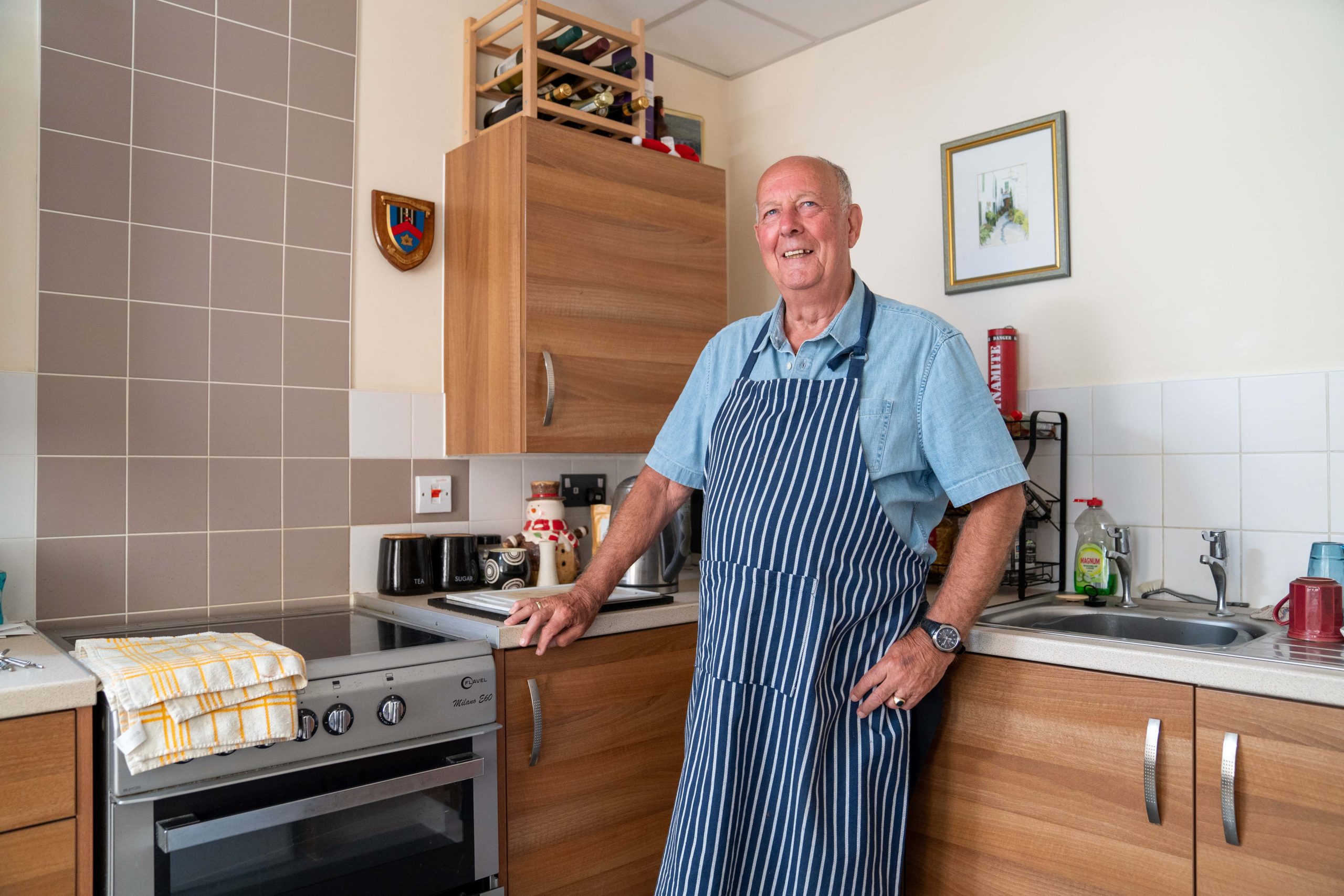 A proud home chef stands with a smile in a well-equipped kitchen, wearing a striped apron and poised for a session of culinary creation.