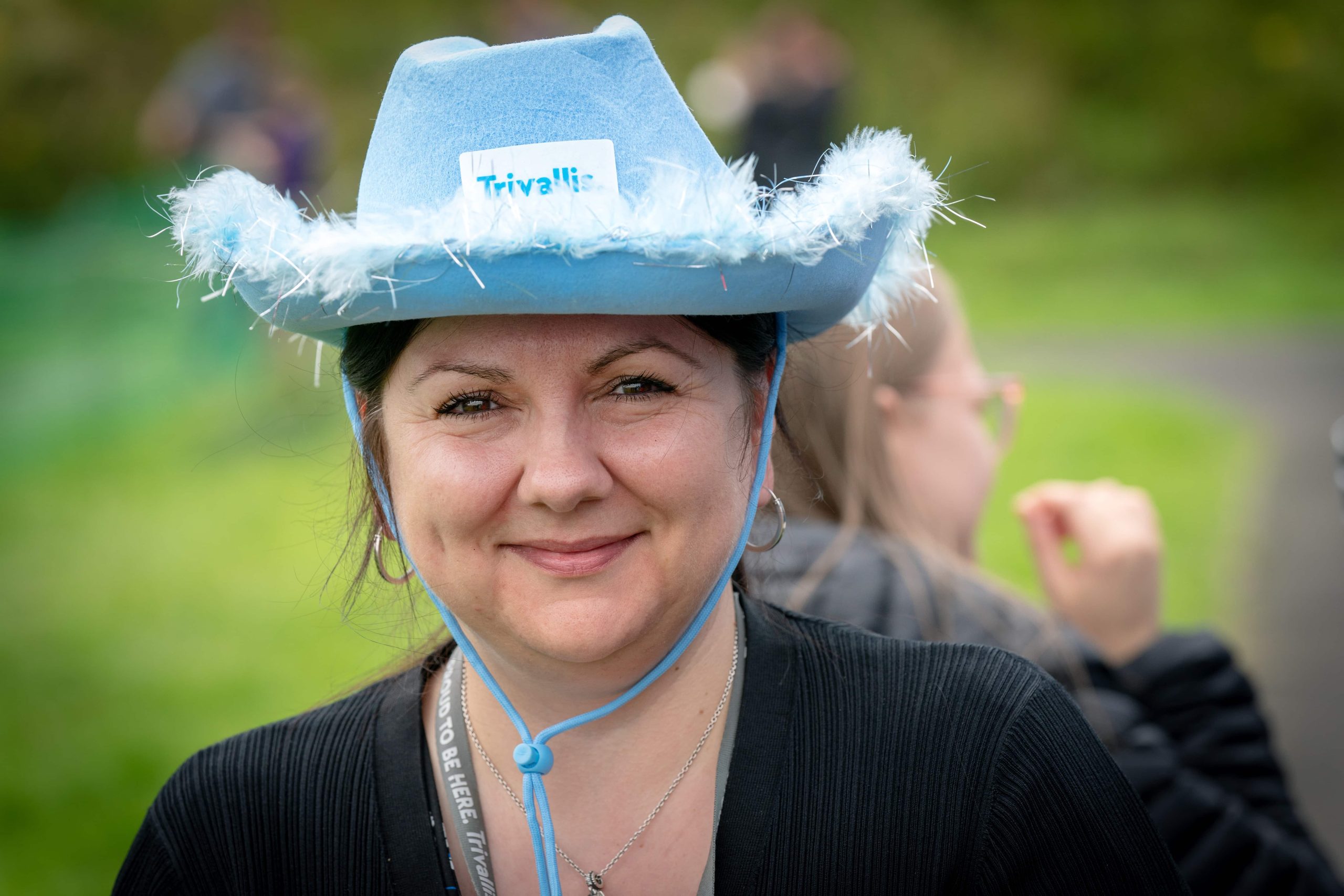 Trivallis Housing Landlord Wales A woman is wearing a blue hat with a "Trivallis!" label and decorative feathers, smiling at the camera.