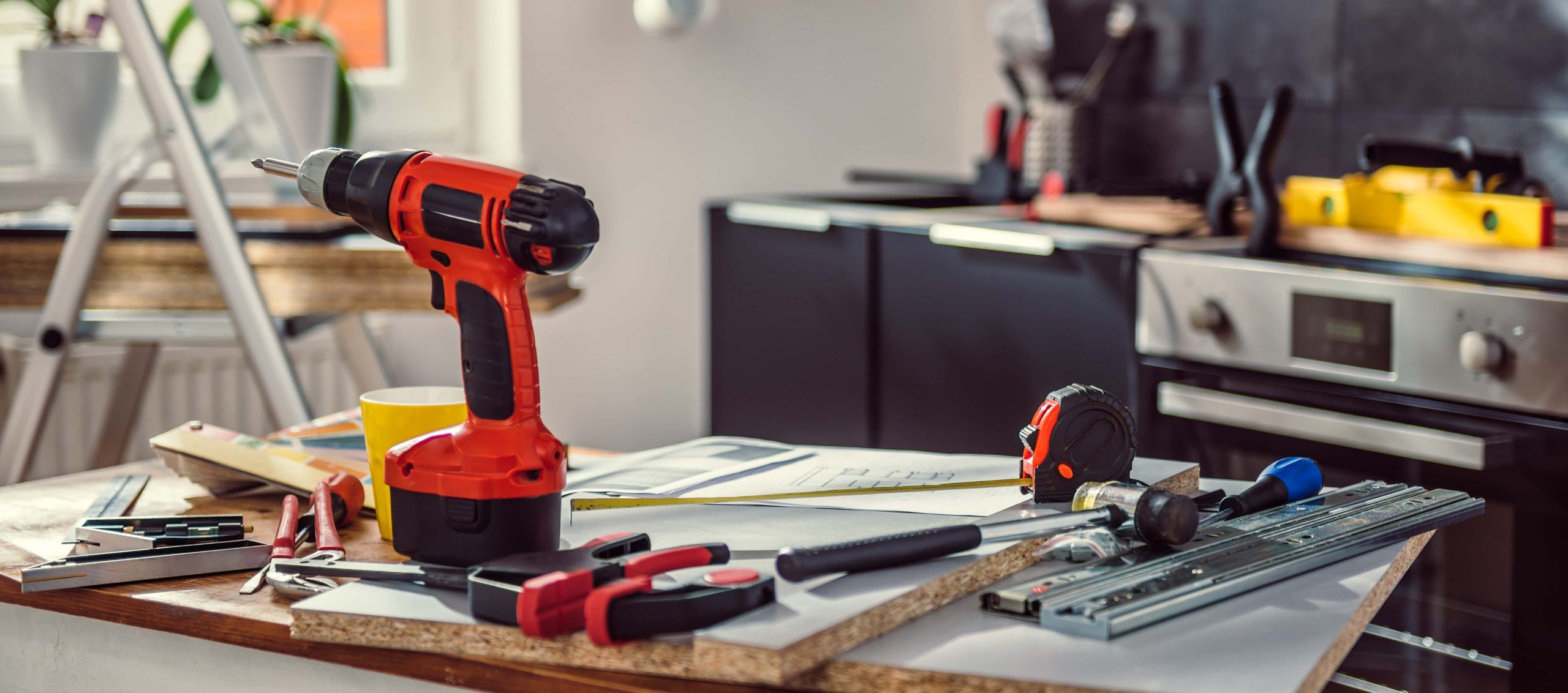 Trivallis Housing Landlord Wales A well-used work surface with various tools, including a cordless drill, tape measure, hammer, and pieces of hardware, suggesting an ongoing planned improvement project in Trivallis homes.