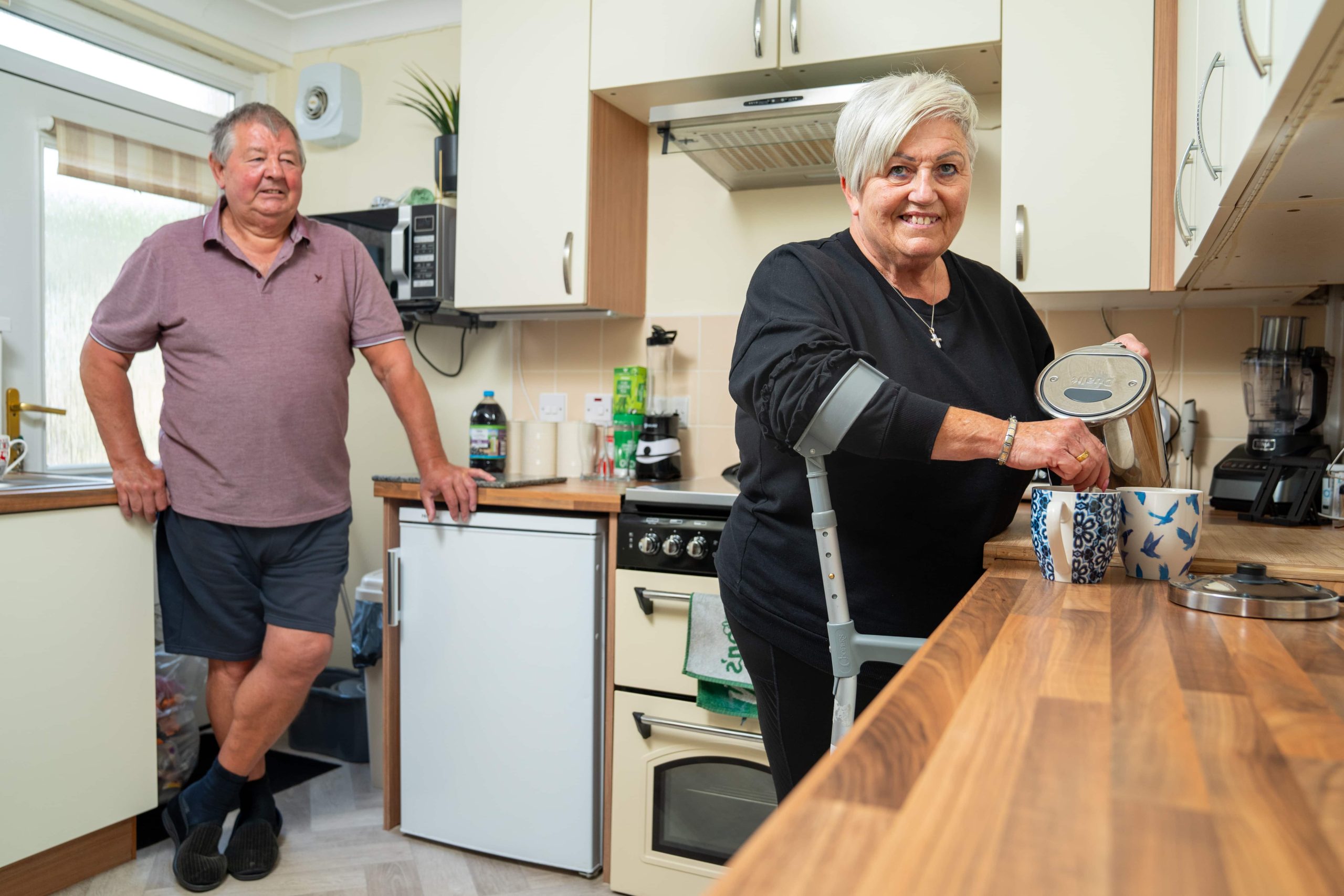 Trivallis Housing Landlord Wales A woman is pouring a beverage from a pot into a cup in a Trivallis kitchen while a man stands in the background observing.