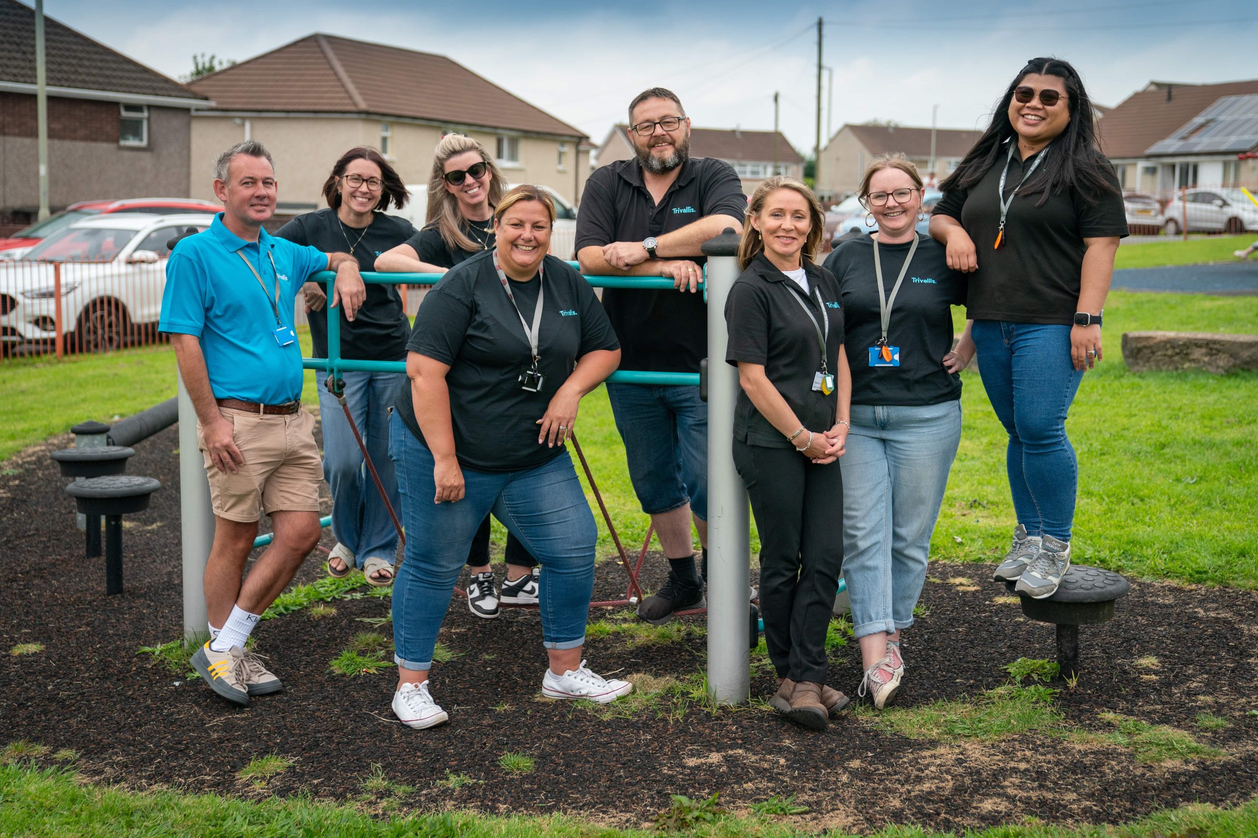 A group of smiling colleagues standing outdoors in a community setting, exuding a team spirit.