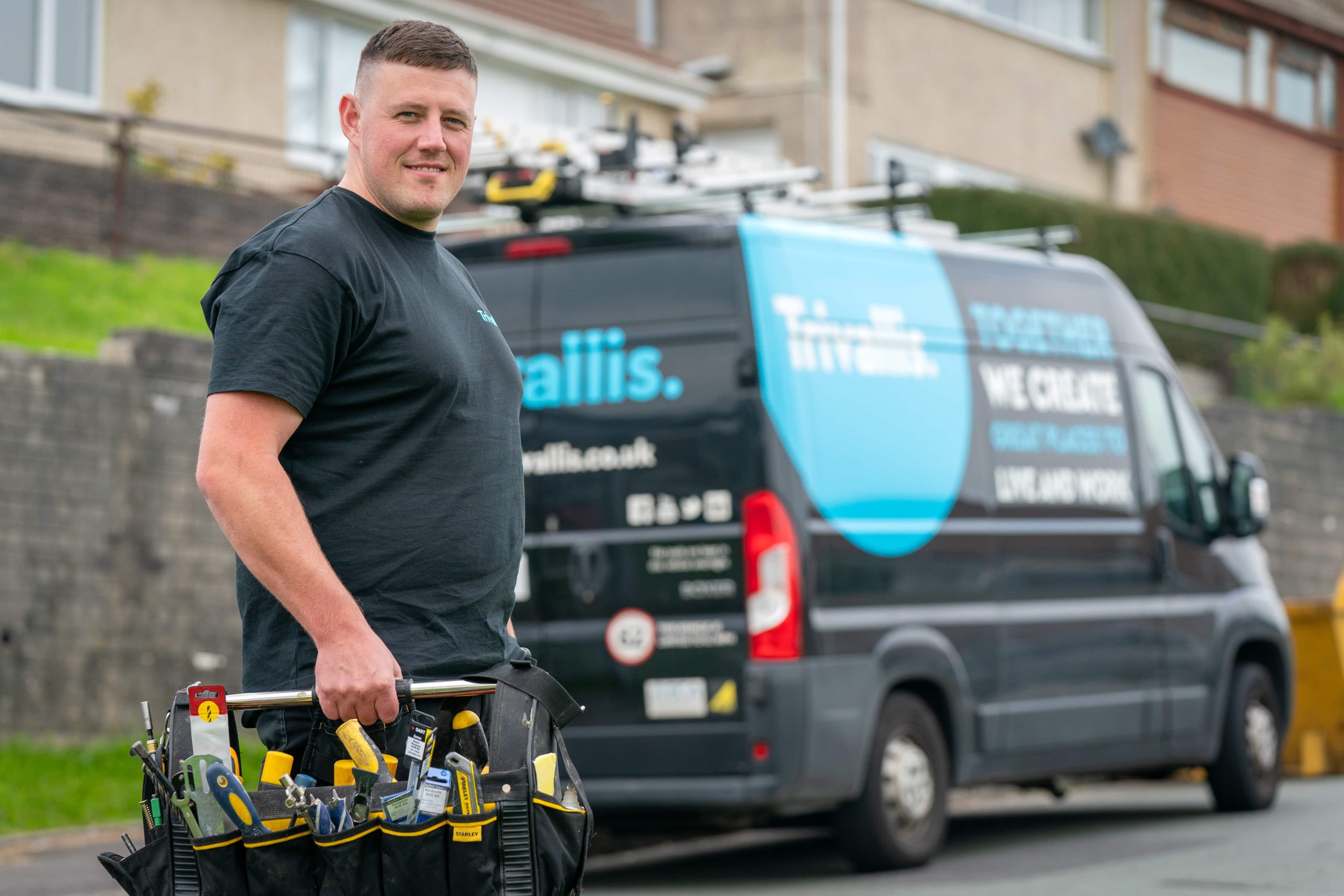 A man carrying a toolbox smiling in front of a service van with 