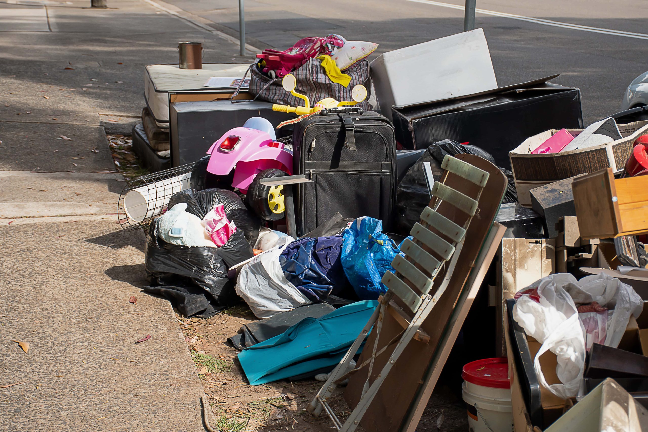 Trivallis Housing Landlord Wales A variety of discarded items, including luggage, furniture, and household goods, piled on a pavement for waste collection. Reporting a waste problem helps us keep things tidy.