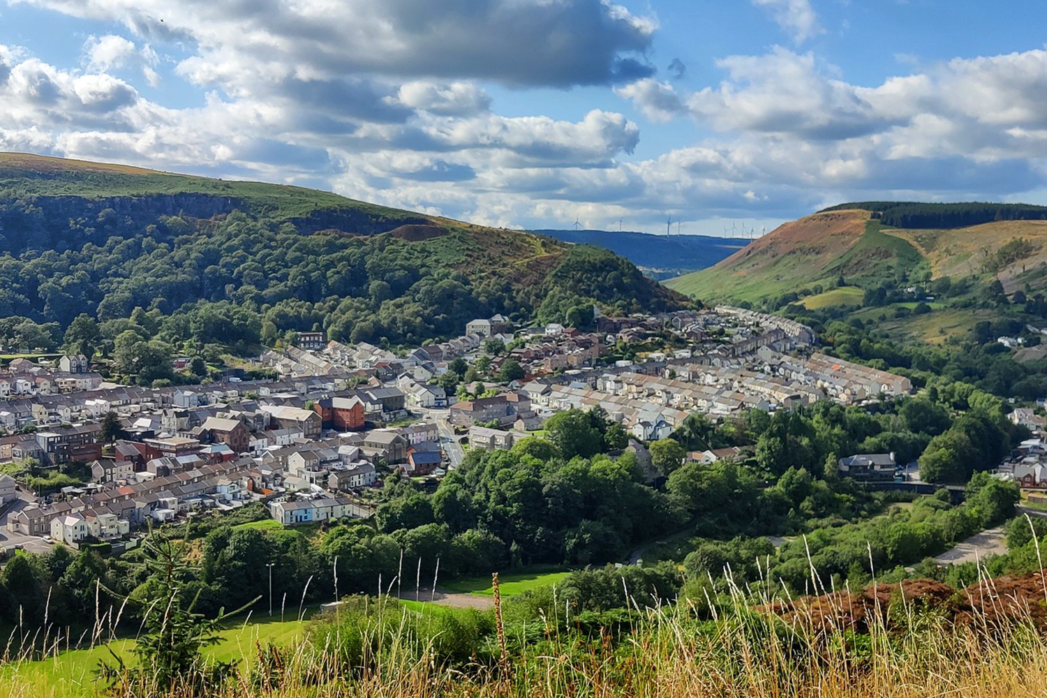 Trivallis Housing Landlord Wales A scenic view of a town nestled in the Rhondda valley with surrounding green hills under a partly cloudy sky, highlighting Trivallis housing.