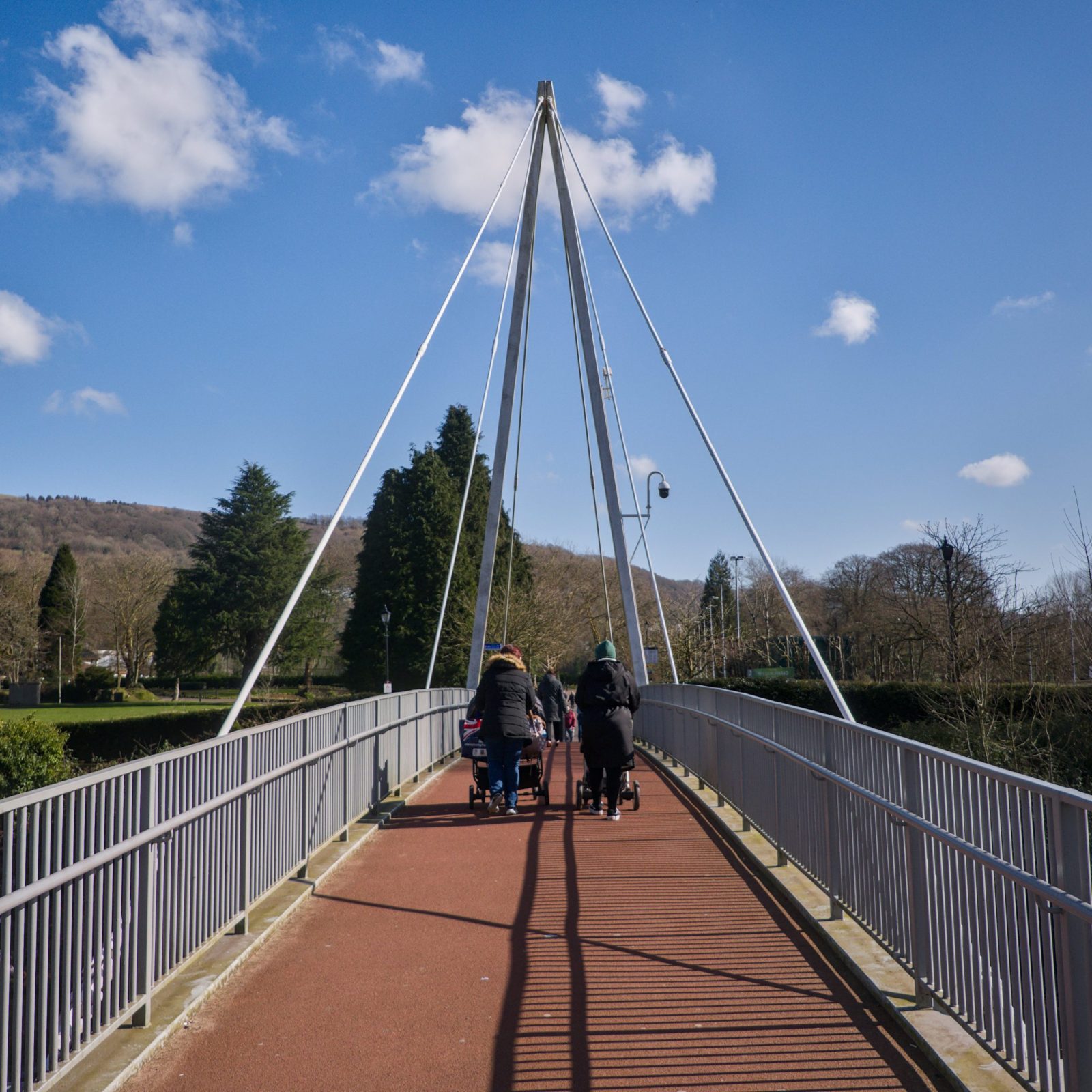 People walking across a modern suspension bridge on a clear day.