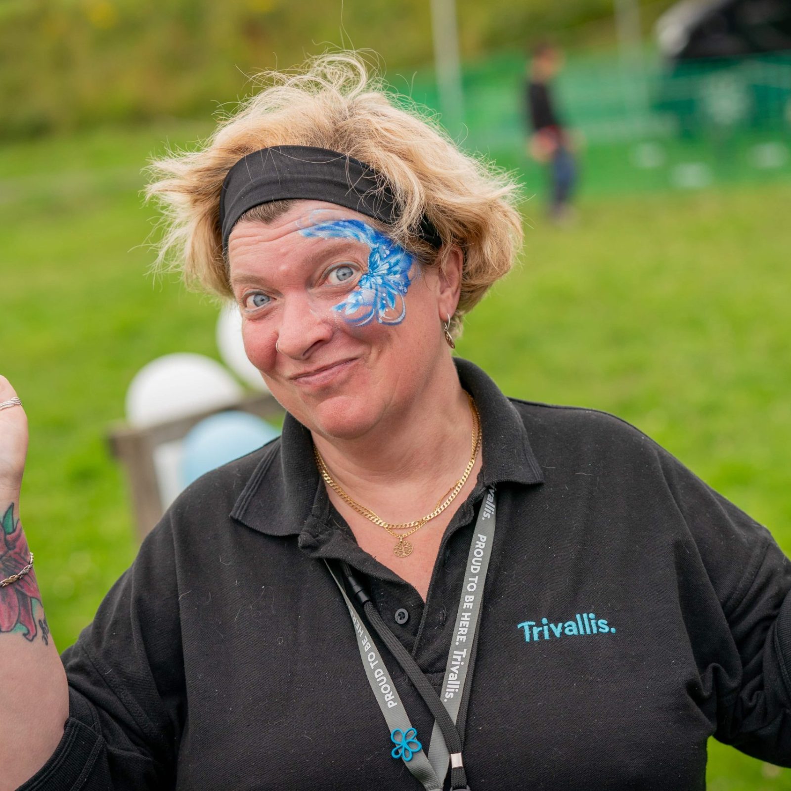 A woman with face paint and a playful expression raises her hands in a whimsical gesture.