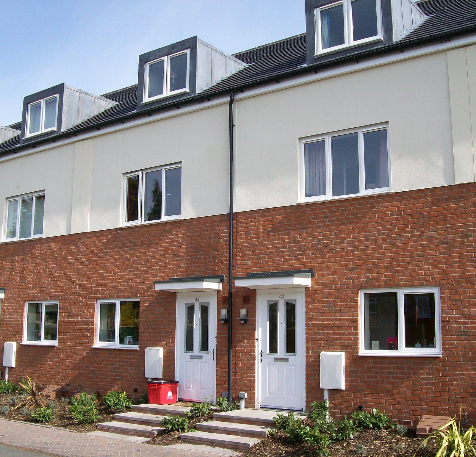 Newly constructed terraced houses with evident brickwork, white doors, and dormer windows under a clear sky.