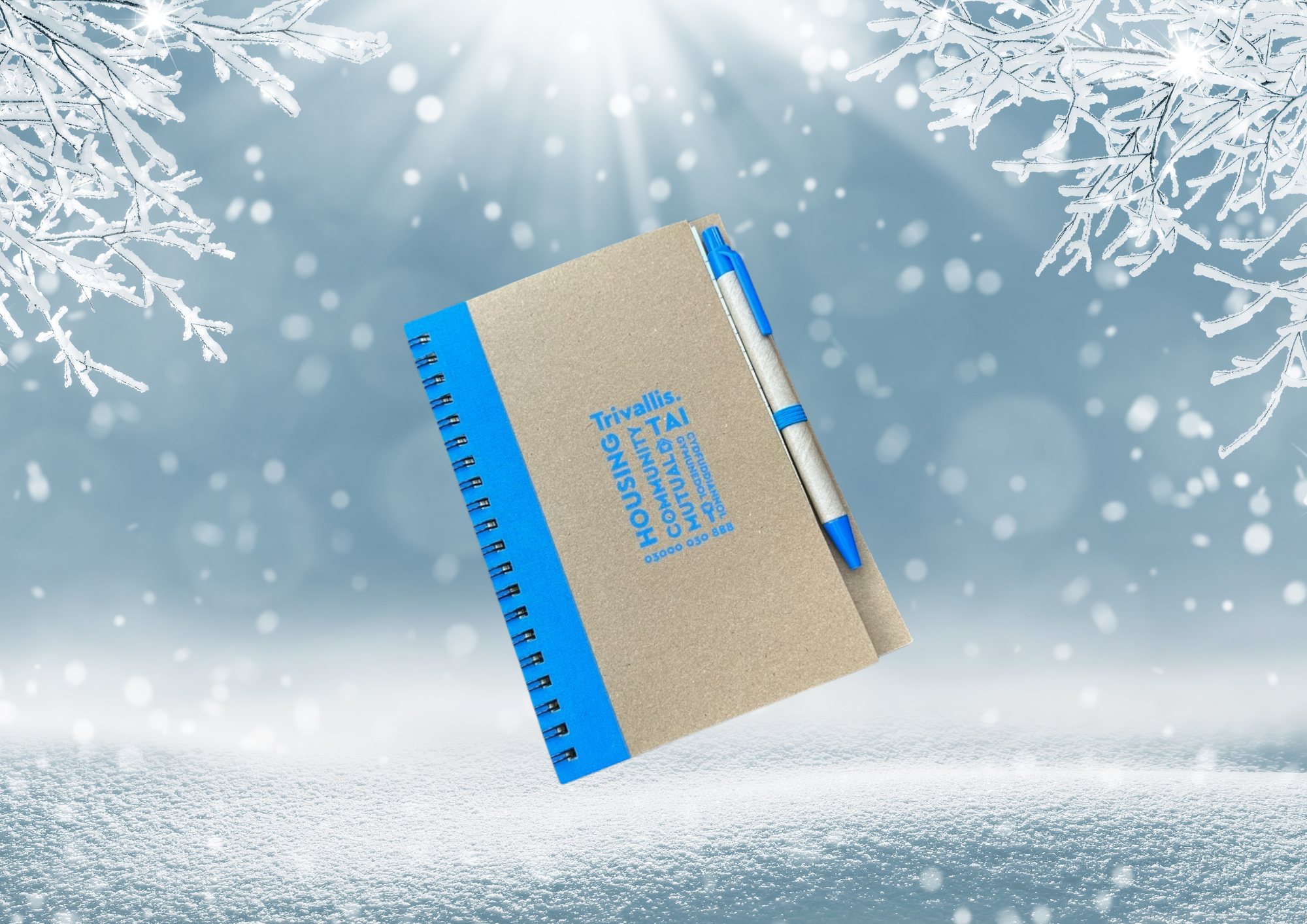 Trivallis Housing Landlord Wales A blue and beige spiral notebook with a pen attached is centered against a winter-themed background with snowflakes and frost-covered branches. The cover has blue text, though it's not fully legible due to image quality.