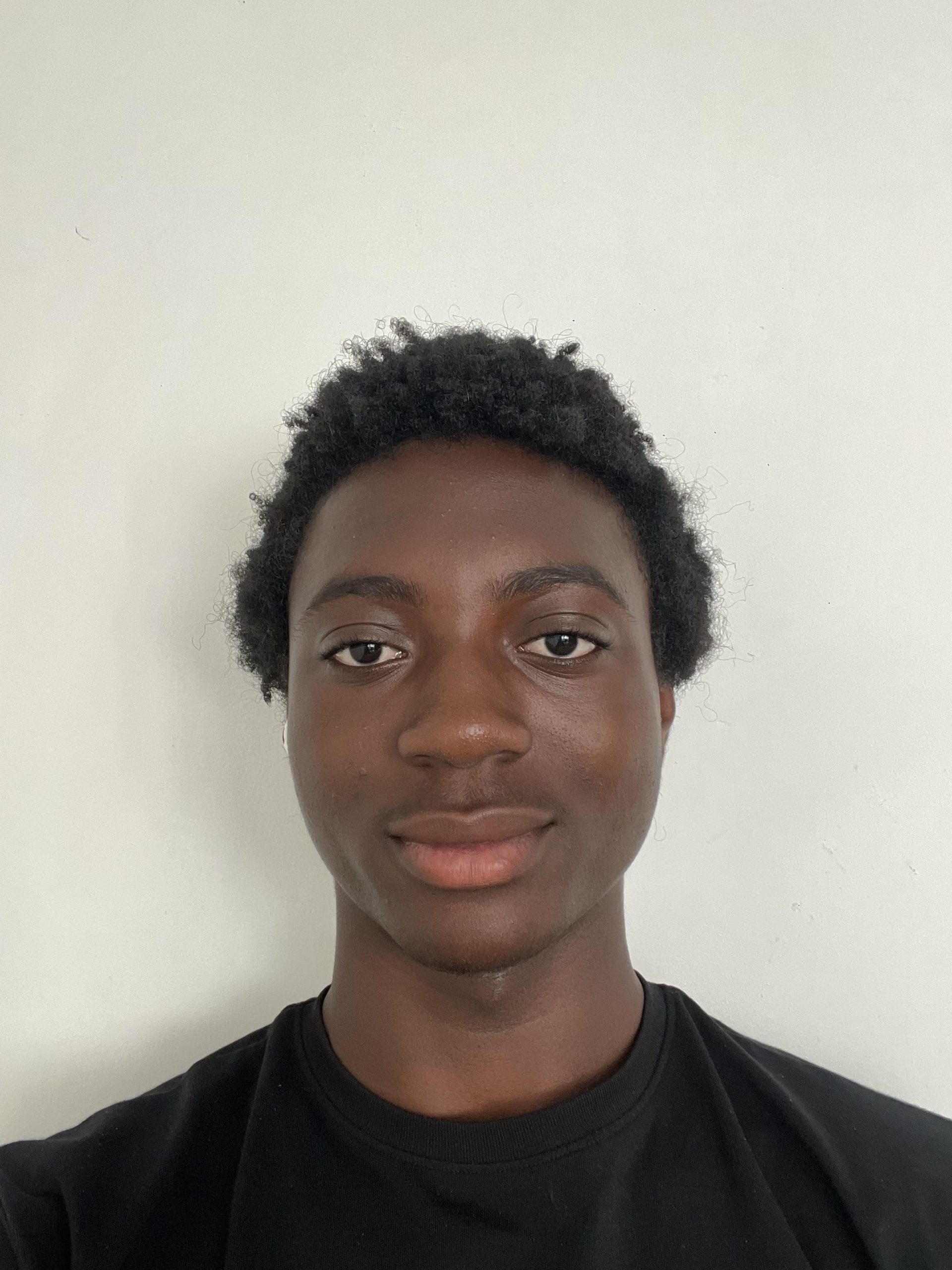 Trivallis Housing Landlord Wales A person with short curly hair and medium-dark skin tone faces the camera and smiles slightly. They are wearing a plain black shirt and standing in front of a plain white background.