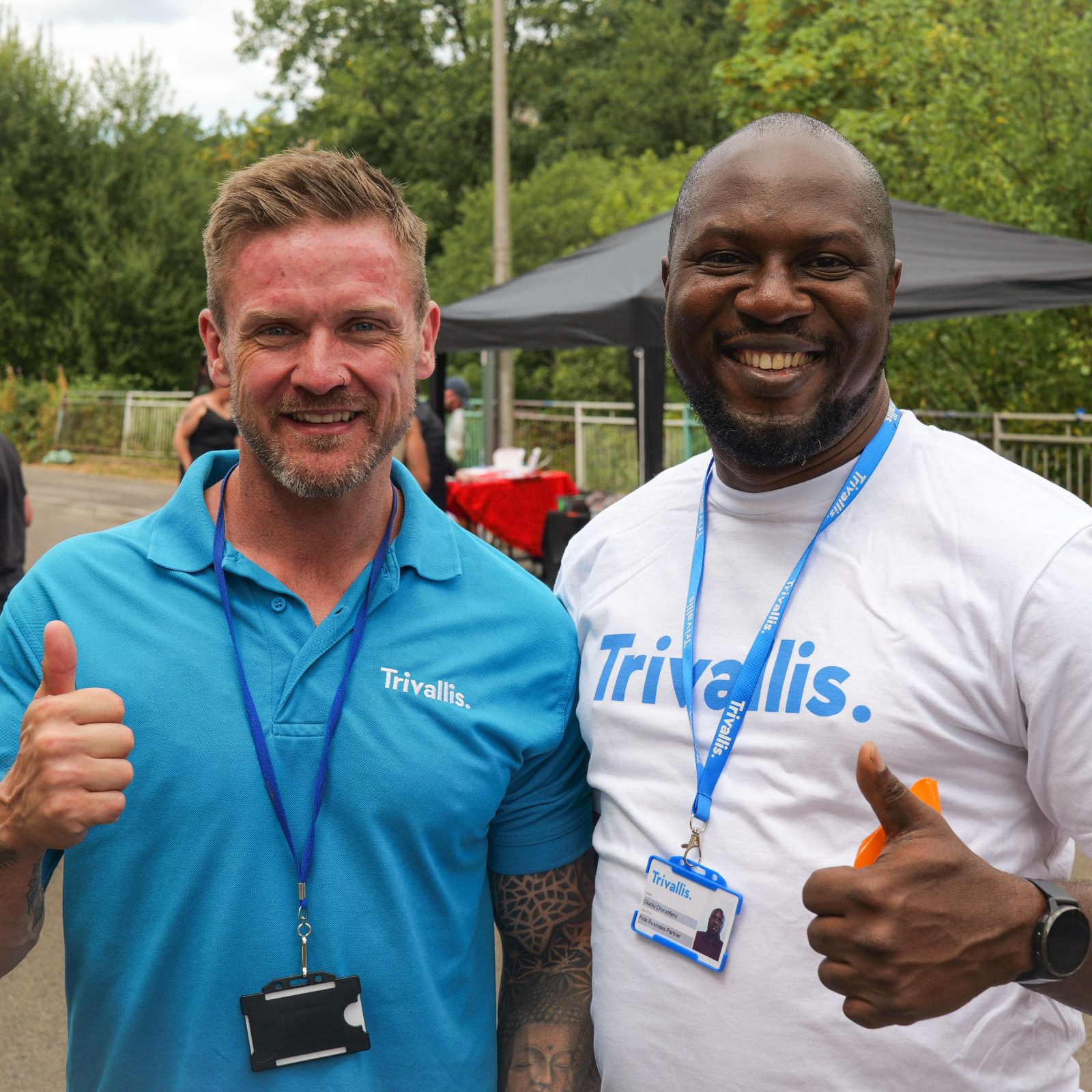 Trivallis Housing Landlord Wales Two men wearing Trivallis branded shirts and lanyards smile and give a thumbs-up.